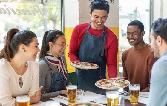 Garçom servindo pizza para clientes no salão